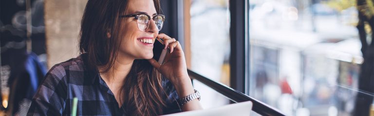 Young woman working on her laptop and talking on mobile phone in cafe